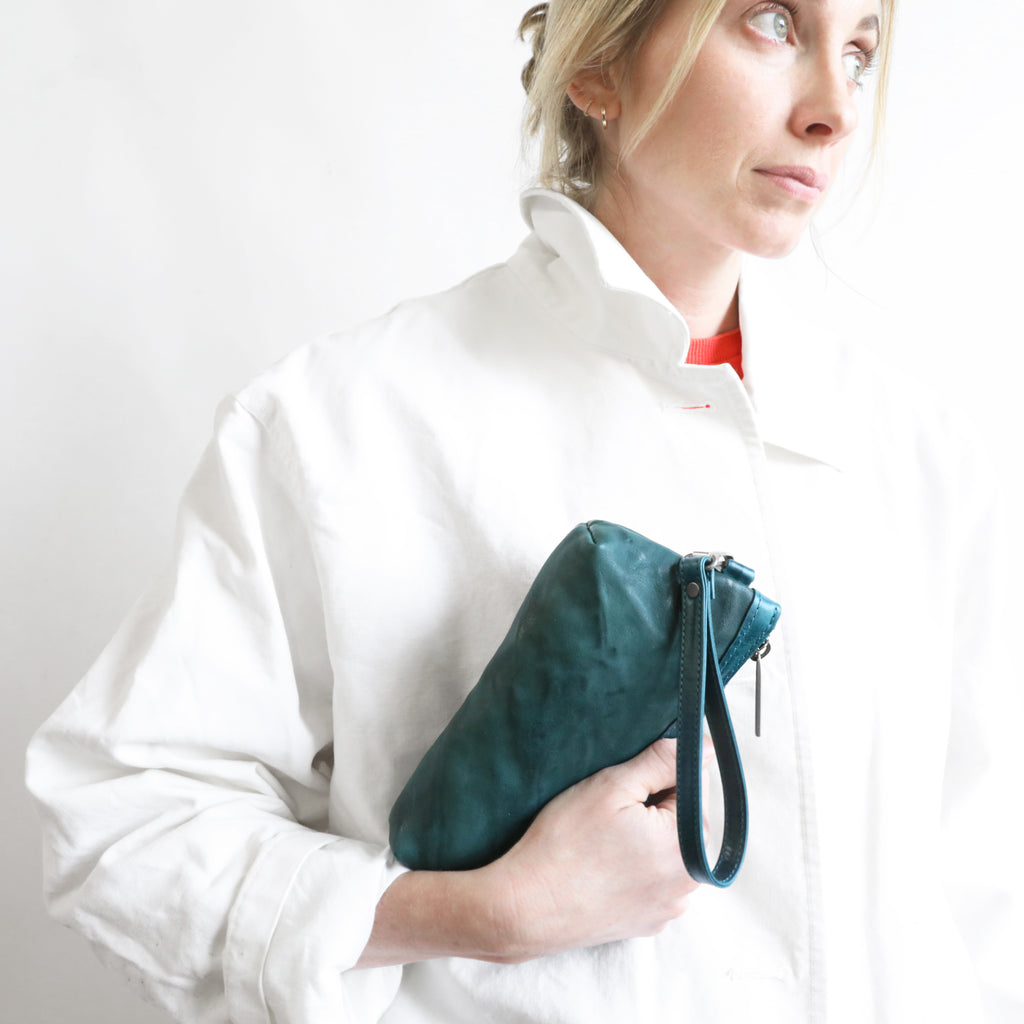 Close-up of model holding a zip pouch medium in rodeo teal and tourmaline. 